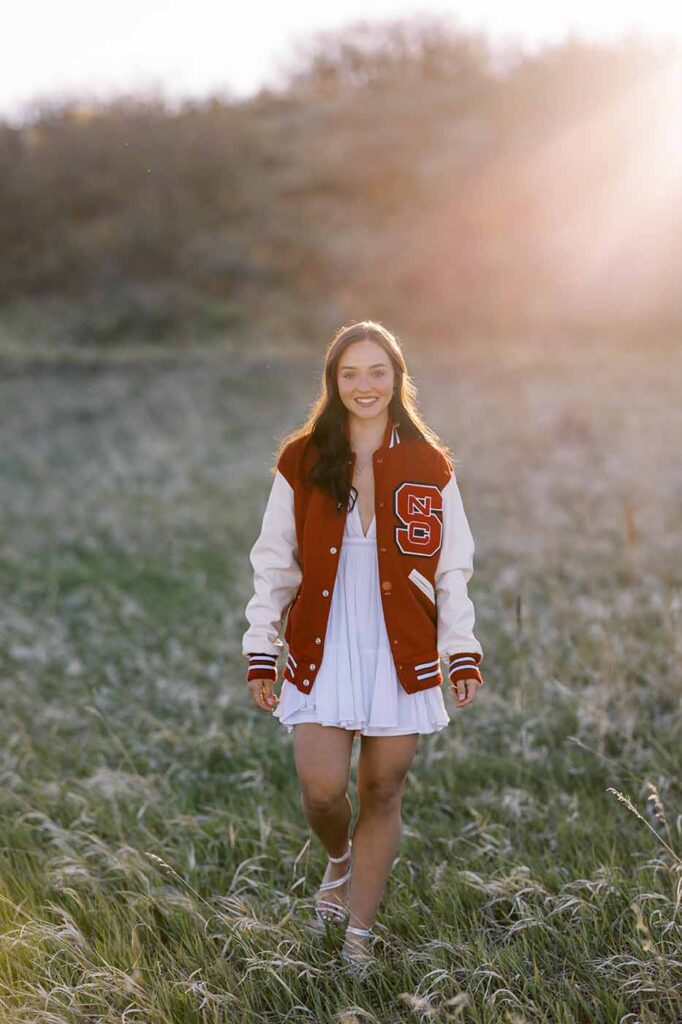 senior graduate girl in white dress walking in grass field in colorado